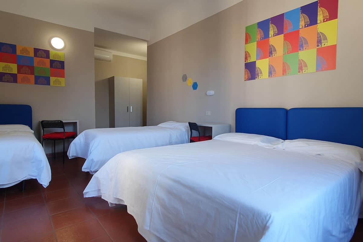 A hotel room with two beds, a desk, a chair, and colorful artwork on the walls.