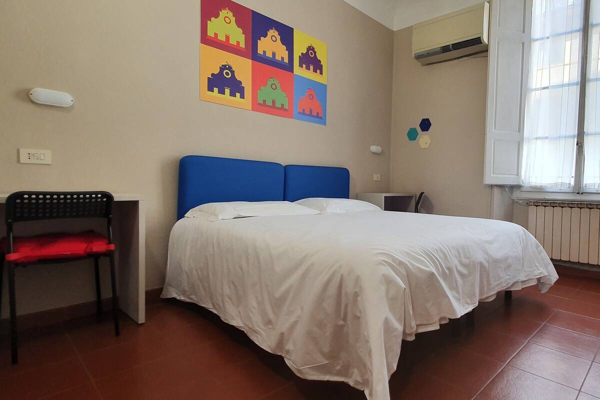 A bedroom with a bed, a chair, a radiator, and a window.