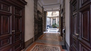 Un pasillo con puertas de madera oscura, suelo de baldosas y vista a un edificio en la distancia.