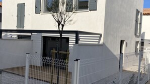 Ein weißes Gebäude mit einem Ziegeldach, einem von einer Mauer umgebenen Innenhof mit einem Baum und einem Metalltor.