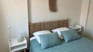 Ein Schlafzimmer mit einem gewobenen Kopfteil, einem Bett mit türkisfarbenen Bettwäsche und einem weißen Nachttisch mit Lampe.