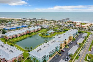 A coastal hotel with multiple buildings, a central pond, and a pier extending into the ocean.