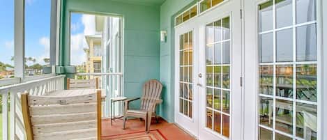 A covered porch with two chairs, a small table, and a view of a building across the street.