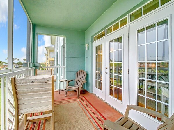 A covered porch with two chairs, a small table, and a view of a building across the street.