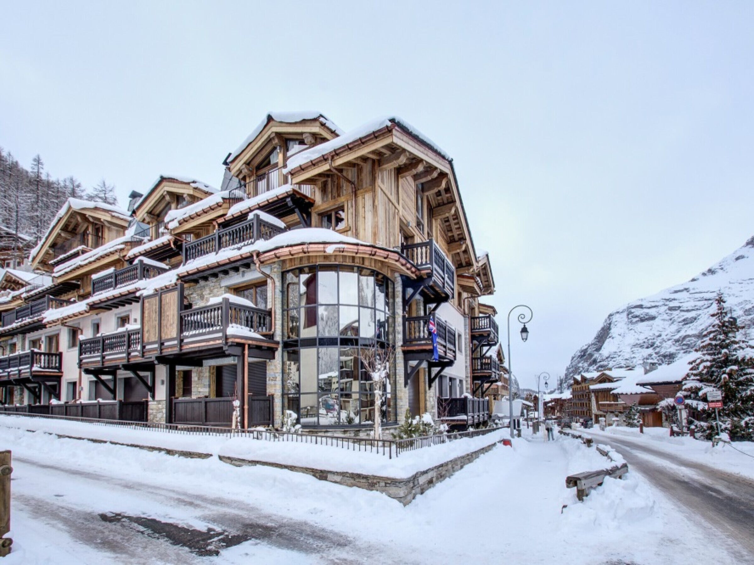 Un bâtiment traditionnel en bois, doté de balcons, de grandes fenêtres et surplombant un paysage enneigé.