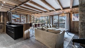 A spacious living area with a wooden ceiling, a sofa, a dining table, and a kitchen area with a bar. - Luxury Apartment with Private Jacuzzi and Stunning Views (Val-d'Isère)
