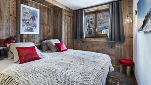 A cozy bedroom with a large bed, wooden walls, a window with a view, and a framed picture on the wall. - Luxury Apartment with Private Jacuzzi and Stunning Views (Val-d'Isère)