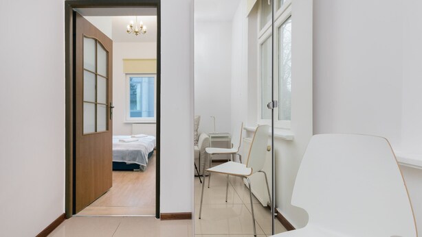 A hallway with a bed, a chair, and a window.