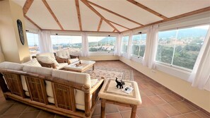 Un solárium con techo alto, ventanas grandes y vista a un paisaje urbano.