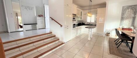 A modern kitchen with white cabinetry, a dining area with a table and chairs, and a staircase leading to another level.
