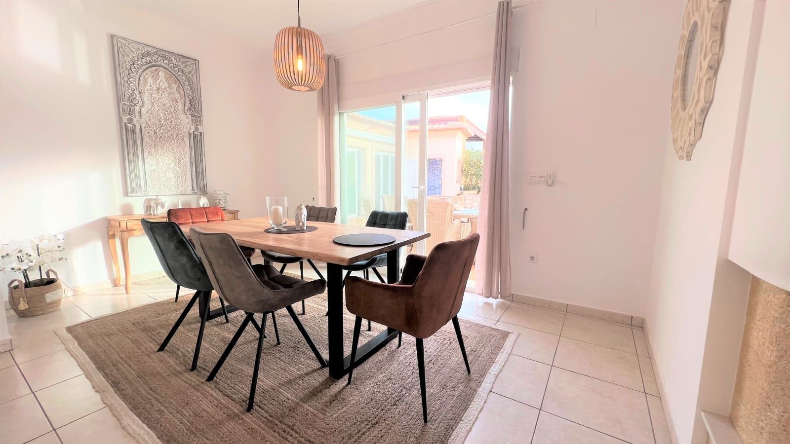 Un espace repas comprenant une table et des chaises, un luminaire suspendu et une vue à travers une porte vitrée.