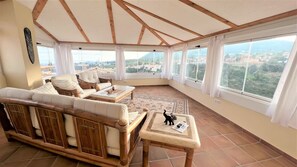 A sunroom with a high ceiling, large windows, and a view of a cityscape.