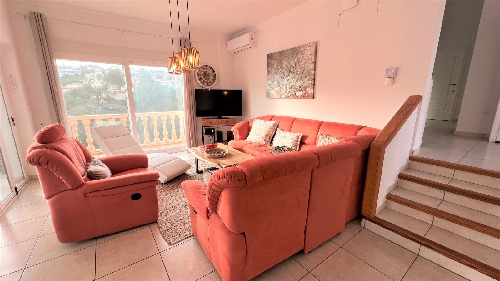 Un salon avec un canapé rose, un fauteuil inclinable, un téléviseur à écran plat et un escalier.