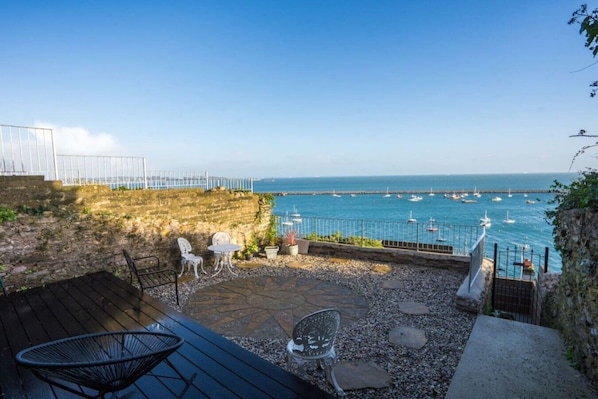 A patio with outdoor seating, a view of the sea, and boats.
