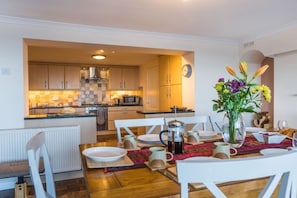 A modern kitchen with wooden cabinets, a microwave, and a dining area with white chairs and a table set for breakfast.