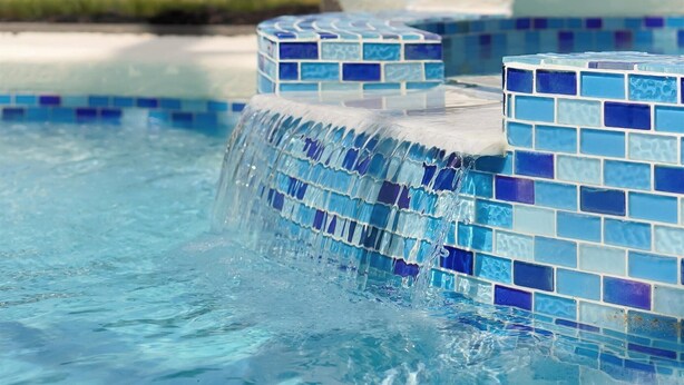 Una piscina con piastrelle blu in mosaico e una piccola cascata.