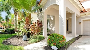 Una casa con portico coperto, garage e giardino curato con diverse piante e una statua di Buddha.