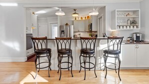 A modern kitchen with white cabinetry, a stainless steel refrigerator, and three bar stools with leather seats. - Beachside Retreat on the Hill (Old Orchard Beach)