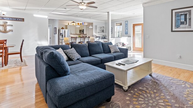 A modern living room with a sectional sofa, a coffee table, and a view of the kitchen and dining area. - Beachside Retreat on the Hill (Old Orchard Beach)
