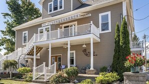 A two-story house with a balcony, a front porch, and a stone pathway leading to the entrance. - Beachside Retreat on the Hill (Old Orchard Beach)