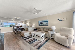 Un vaste espace de vie comprenant un ventilateur de plafond, une table à manger avec des chaises, un canapé, un fauteuil et un tapis.