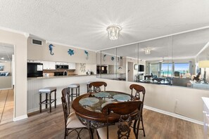 A modern kitchen with a central island, bar stools, and a dining table with chairs.