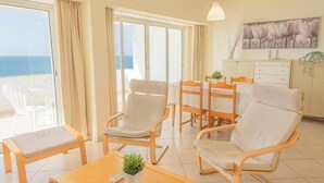 Une chambre d’hôtel moderne dotée d’un balcon, d’un coin repas et d’un espace de vie comprenant un canapé et des fauteuils.