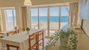 Un coin repas avec une table dressée pour deux personnes, une plante en pot et une vue sur la mer grâce à de grandes portes coulissantes.