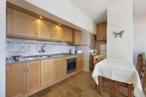 A compact kitchen with wooden cabinets, a built-in oven, and a dining area with a table and chairs. - Apartamentos Rocha Praia Mar (Portimão)