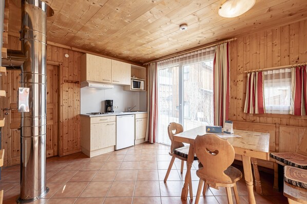 Interior de madera con cocina, comedor y un amplio ventanal con cortinas.