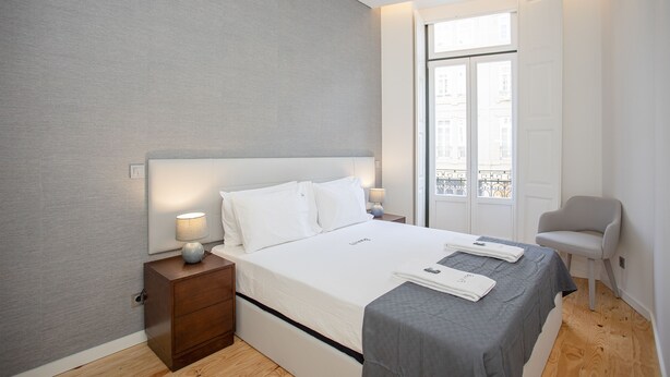 A modern bedroom with a large bed, bedside tables, a chair, and a window with a view. - Liiiving-Mouzinho Residence Apartment 1F (Porto)