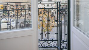 A balcony with wrought iron railings, a view of buildings, and a tree with yellow leaves. - Liiiving-Mouzinho Residence Apartment 1F (Porto)