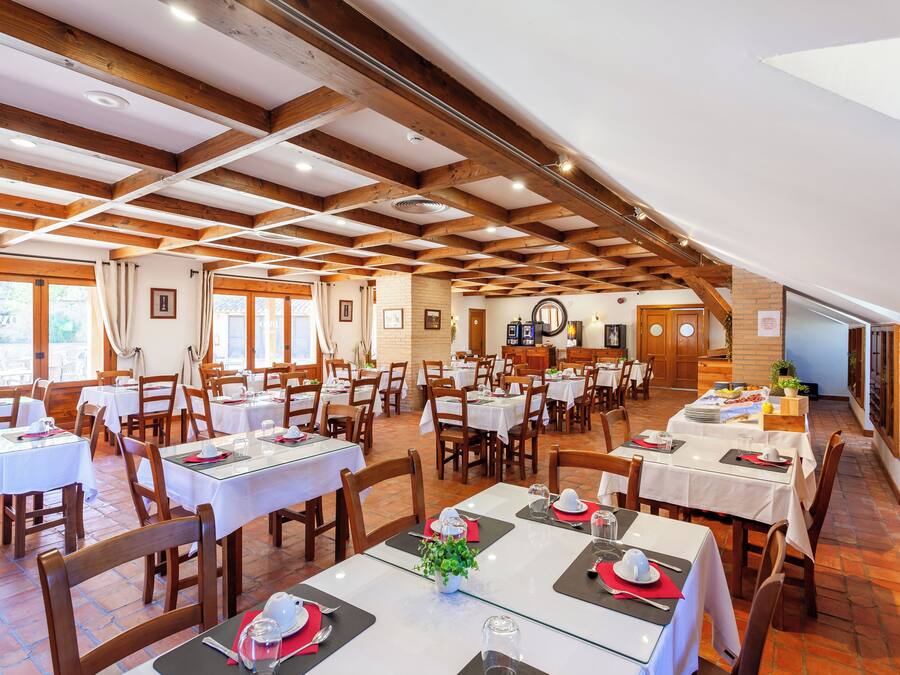 Un restaurante con varias mesas y sillas, vigas de madera en el techo y una pared de ladrillo.