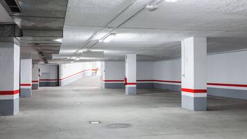 Un parking à plusieurs niveaux aux murs blancs et aux bandes rouges, doté de piliers en béton et d’une allée centrale.