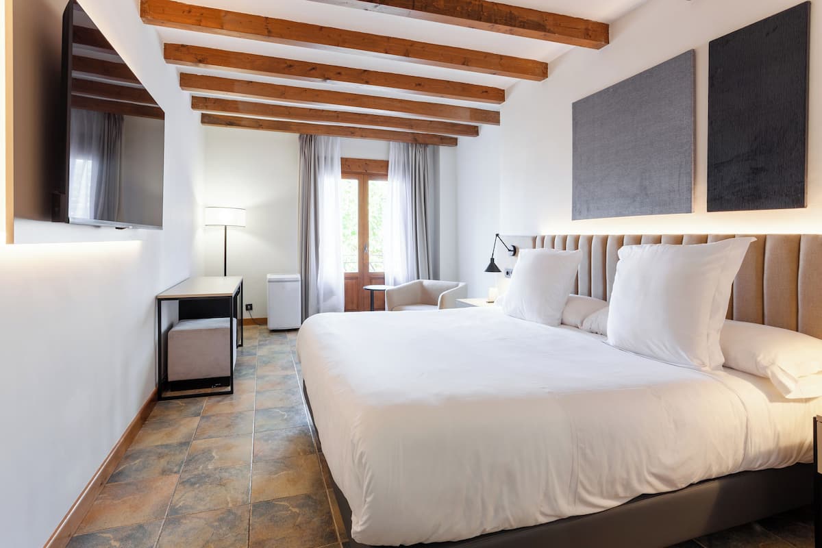 Een moderne hotelkamer met een groot bed, houten balken, een flatscreen televisie, een bureau en een raam met gordijnen.