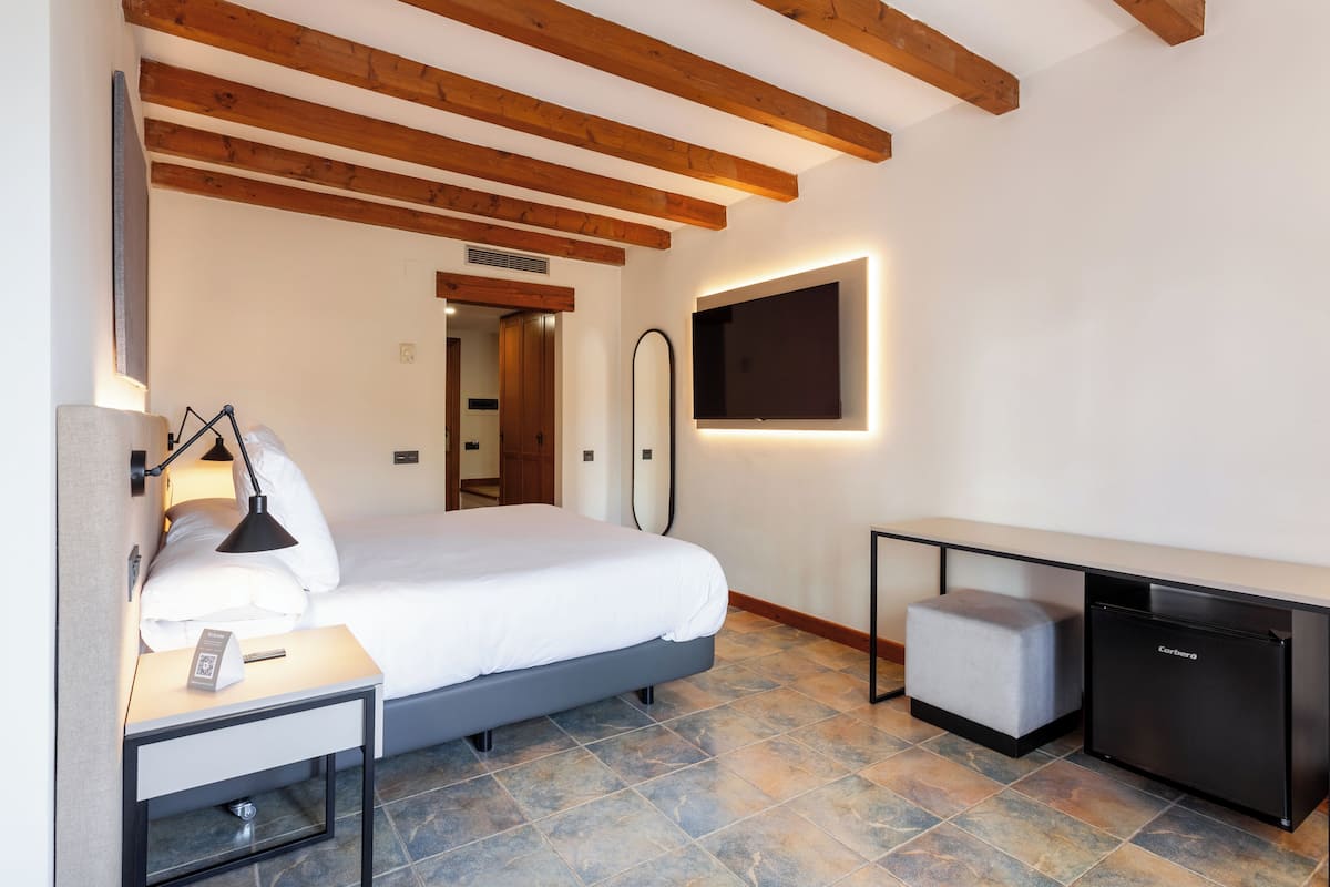 Een moderne hotelkamer met een bed, nachtkastje, lamp en een kleine, zwarte koelkast.