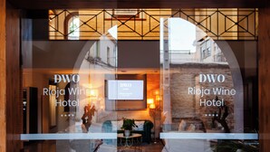 The entrance of the DWO Roja Wine Hotel with a glass facade, interior seating area, and a stone wall.