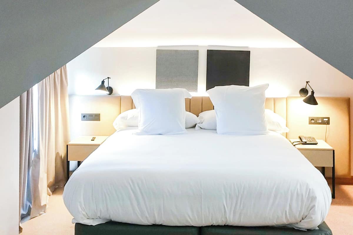 Een hotelkamer met een groot bed, twee nachtkastjes, een lamp en uitzicht op de lucht.