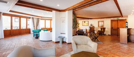 A spacious living area with a high ceiling, wooden beams, and a large window overlooking a balcony.