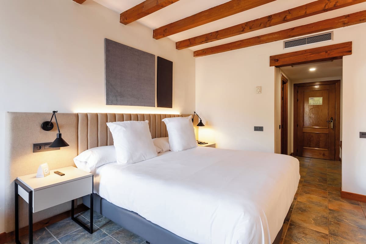 Een slaapkamer met een groot bed, twee nachtkastjes met lampen, een houten plafond en een deur naar een andere kamer.