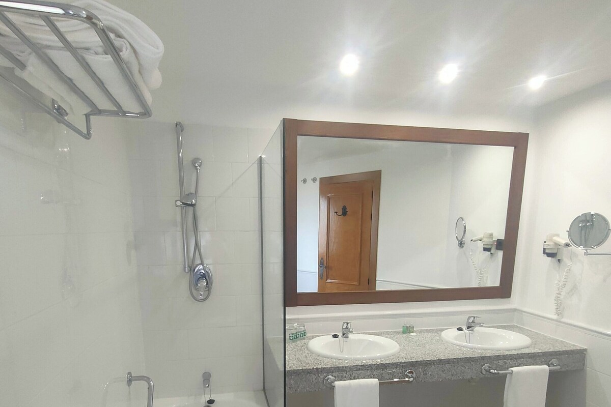 Une salle de bain avec une baignoire, deux lavabos, un grand miroir et un espace douche.