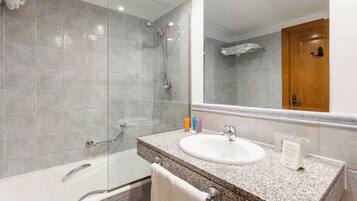 A modern bathroom with a glass-enclosed shower, a white bathtub, and a granite countertop sink.