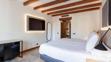 A bedroom with a bed, bedside lamp, and a small desk with a refrigerator.