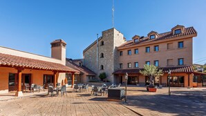 Une cour avec des sièges en plein air, un bâtiment en pierre doté d’une tour et un bâtiment moderne avec de nombreuses fenêtres.