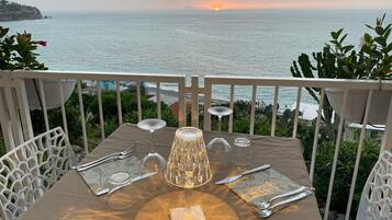 A table set for two with a view of the sea and a sunset in the background.