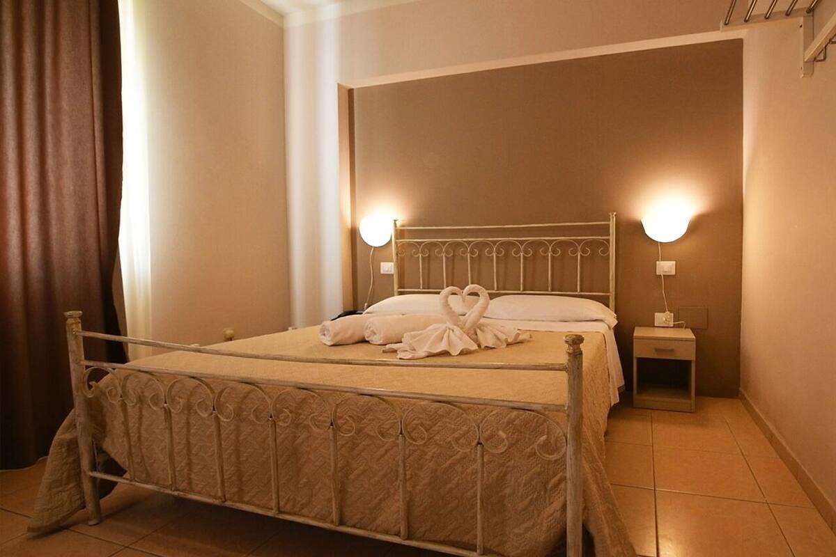 A neatly made bed with a heart-shaped towel arrangement, two bedside lamps, and a small bedside table.