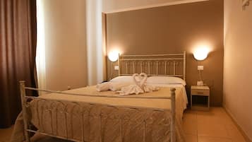 A neatly made bed with a heart-shaped towel arrangement, two bedside lamps, and a small bedside table.