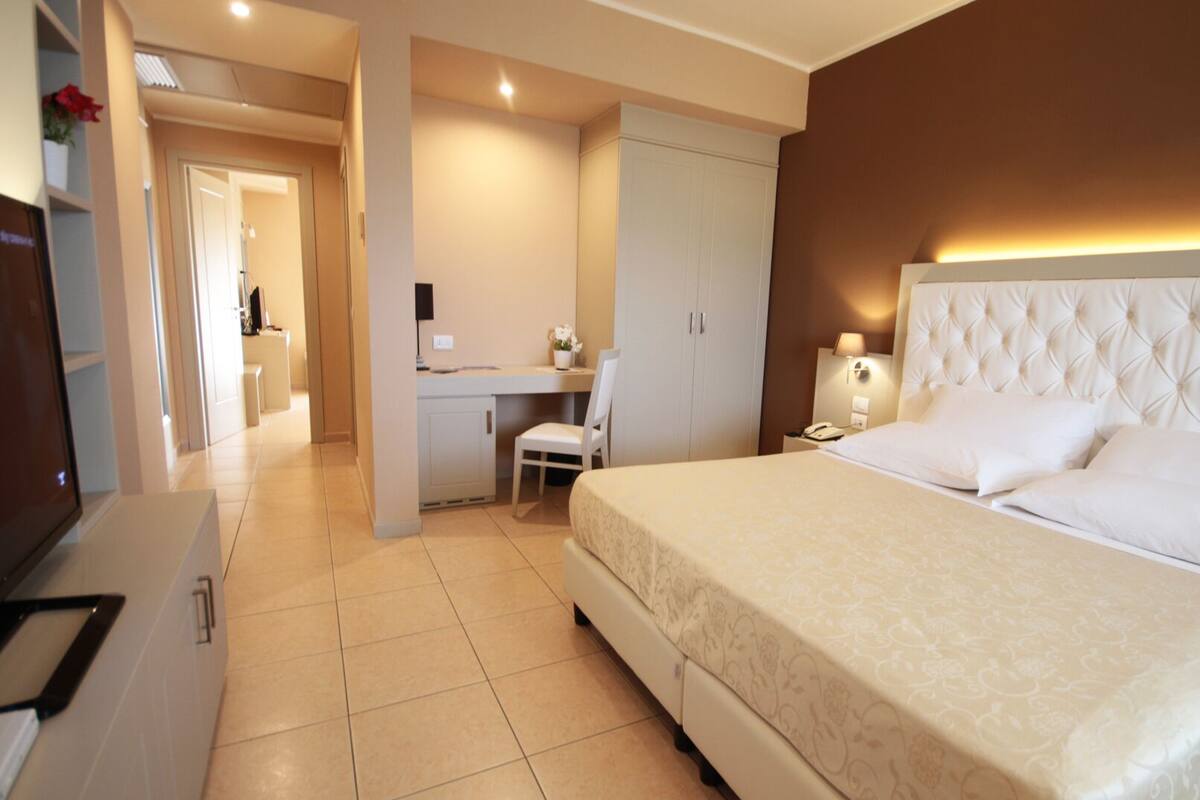 A hotel room with a large bed, a desk, and a chair.