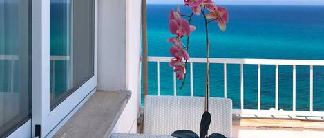 Un balcon donnant sur l’océan, une orchidée en pot et une paire de lunettes de soleil posées sur un tapis tressé.