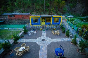 Un bâtiment à la façade jaune et bleue, entouré d’une zone pavée avec des espaces de repos extérieurs et un motif en forme de croix en pierre.